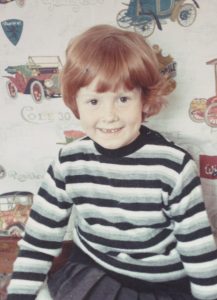 Image of KATHARINE CAROL, Artistic and Executive Director when she was a baby in a striped shirt