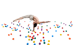 man performing a handstand with colorful plastic balls laid out on the floor