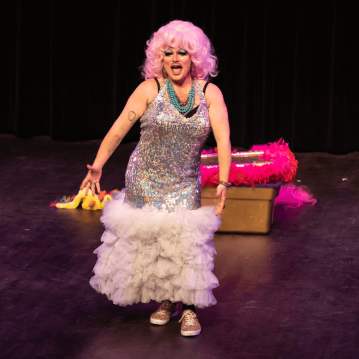 a drag performer on stage in a silver sequin dress