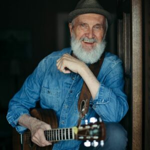 Fred Penner from ‘The Cat Came Back’ performance wearing a denim shirt and grey fedora smiling at the camera