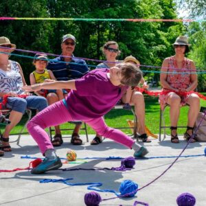 Image of person dressed in pink doing the limbo under multi-coloured yarn during our Tricoter dance performance. Join us on May 31st-June 5th