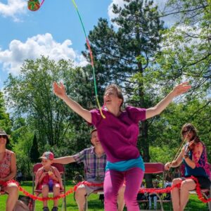 Image of woman in purple throwing a ball of yarn into the air with her arms up and smiling during our Tricoter performance