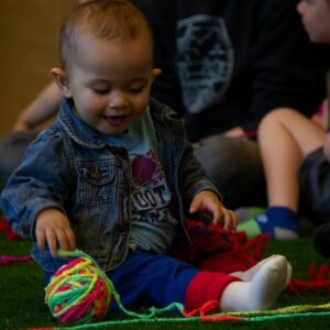 Image of young child smiling and looking at a ball of multicoloured yarn