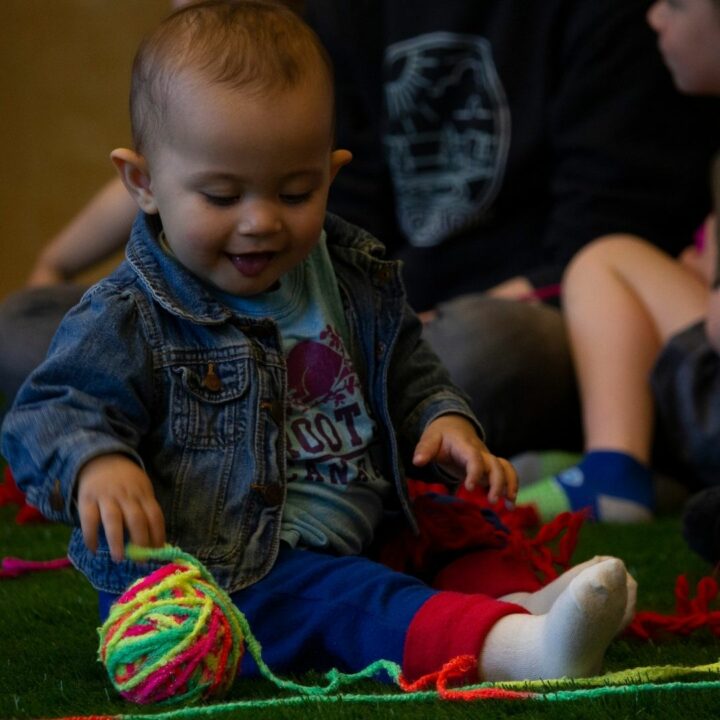 Image of young child smiling and looking at a ball of multicoloured yarn