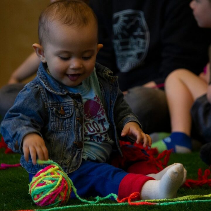 Image of young child smiling and looking at a ball of multicoloured yarn