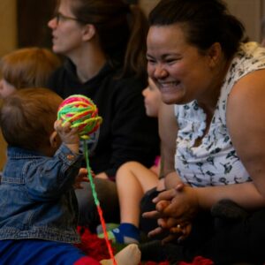 Image of woman smiling at a young child holding a ball of multicoloured yarn up
