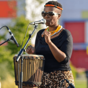 Image of a performer from the Africa Oyé performance singing and drumming into microphones in the sunshine
