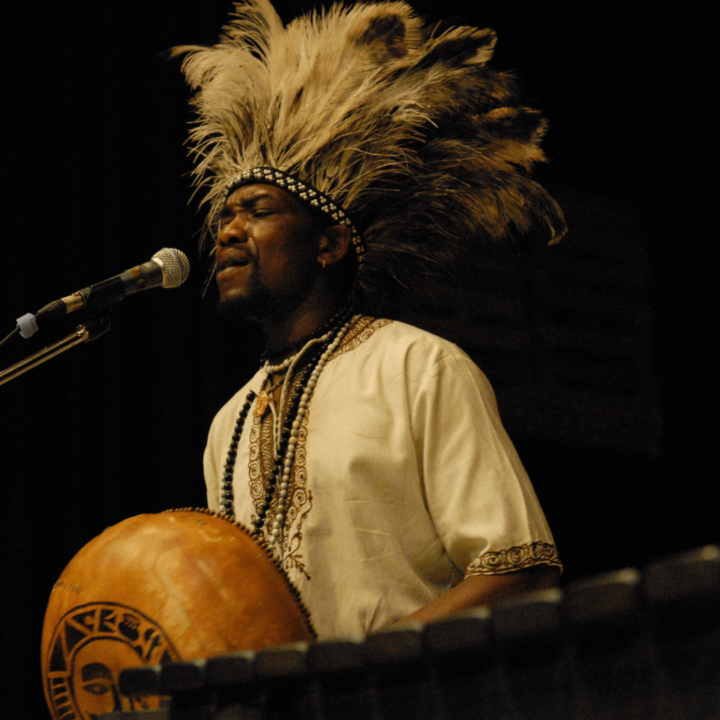 Image of performer from the Africa Oyé performance wearing a feather head ornament singing into a microphone