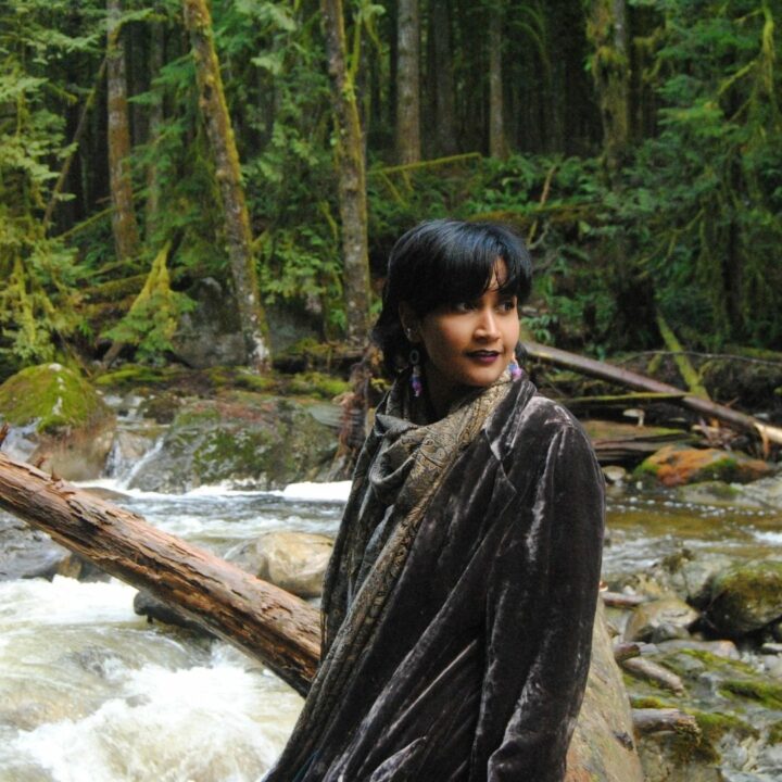 Image of Anjalica Solomon standing in the forest. They are a featured artist in the future artists performance on June 3rd