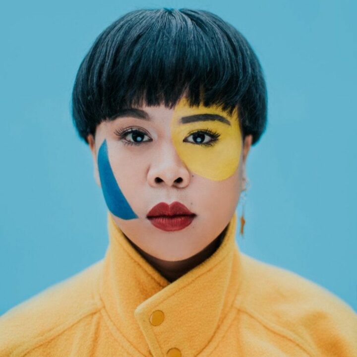 Image of Kimmoral with blue and yellow face paint. They are a featured artist in the future artists performance on June 3rd