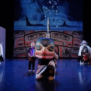 Whales Dancers of Damelahamid - Indigenous dancer crouching and holding a wooden whale mask.