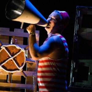 Image of performer in red and white stripes singing into a megaphone. From The Girl who Forgot to Sing Badly performance, available online from May 31st-June 12th