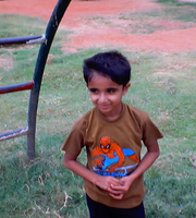 A childhood photo of one of our board members, Samad Raza, standing on a grass field and smiling, while wearing a Spiderman shirt.