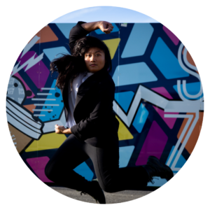 Image of Find Mutya jumping in the air in front of street art. She is a featured artist in the future artists performance on June 3rd