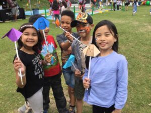 Children smiling with face paint and holding up crafts created in our activity village