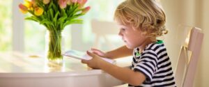 Child in striped shirt, sitting at table using a tablet