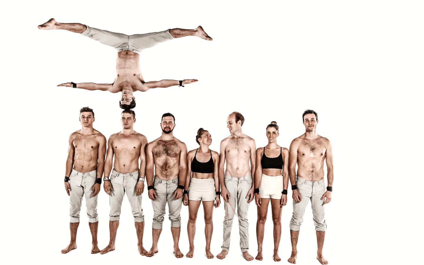 8 acrobatic performers standing next to each other, with one of them balancing upside down on another performer's head.