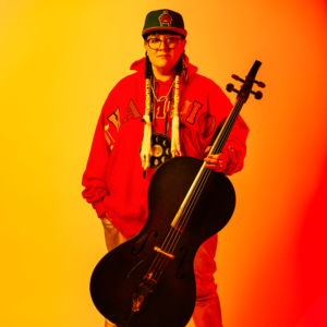 Cris Derken holding a cello, while standing in front of an orange backdrop
