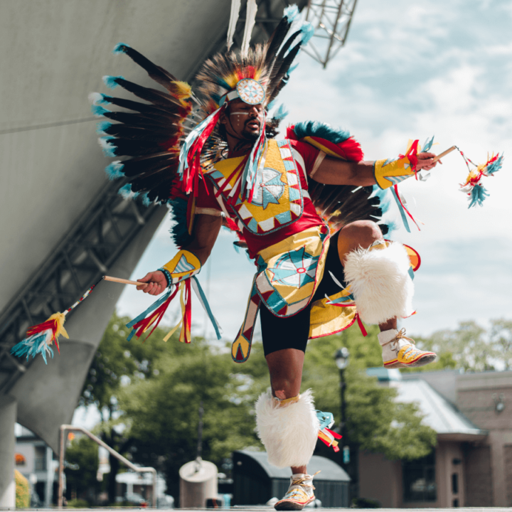one of the dancers from the dance group The Wild Moccasin Dancers, dancing on stage and wearing Indigenous regalia