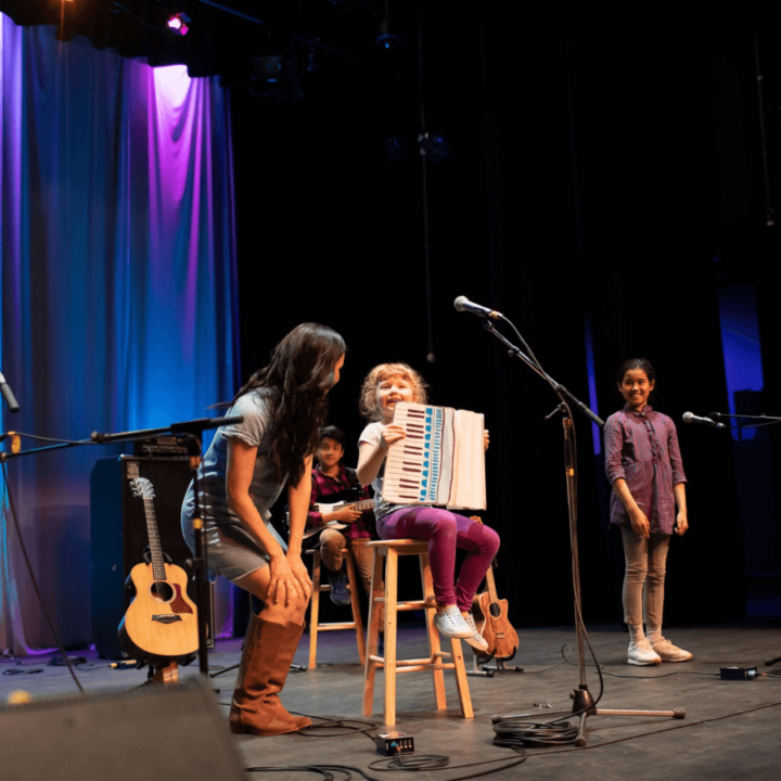 Ginalina on stage with a child holding an accordion sitting next to them on a stool