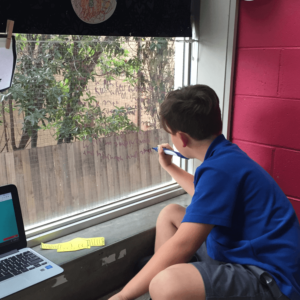 a child writing on a glass window with a marker, with trees in the background
