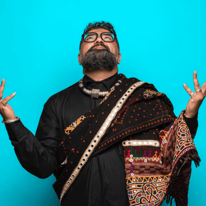 one of our performers Ruploops wearing a black shirt and shawl looking up, with a blue background