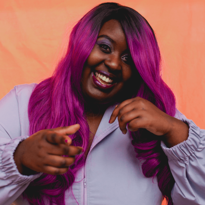 Missy D smiling and wearing a light purple jacket, with a orange background