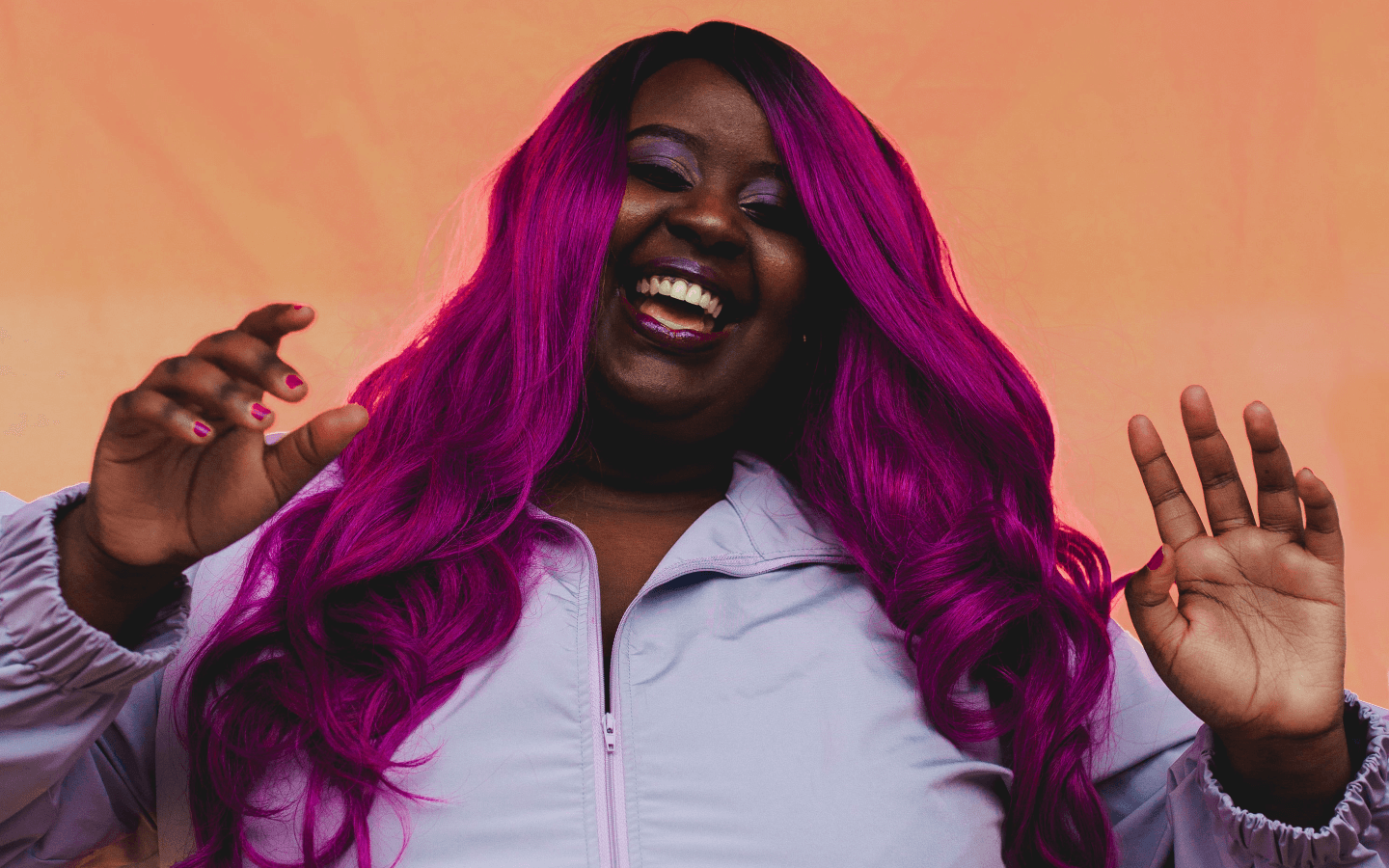 Missy D smiling with both hands in the air, while wearing a light purple jacket