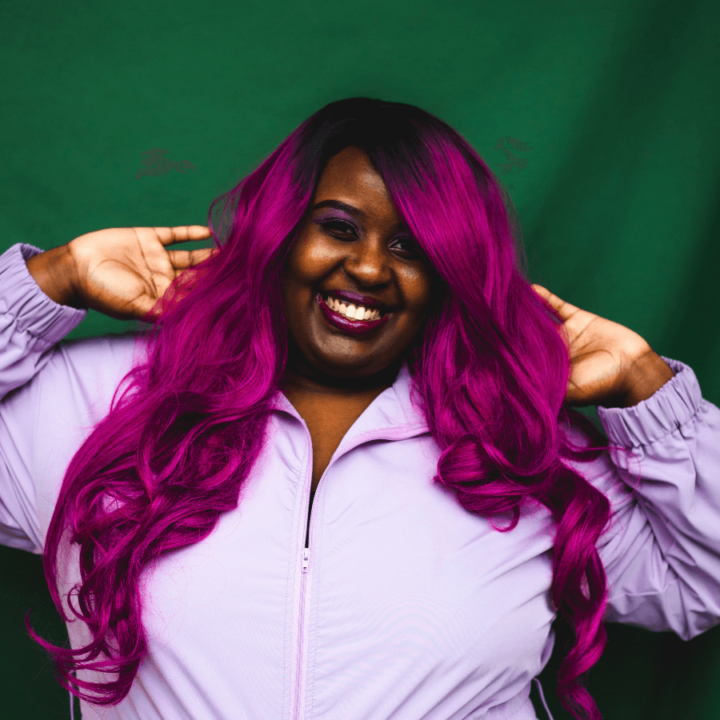 Missy D, smiling and wearing a light purple jacket, and standing in front of a green backdrop