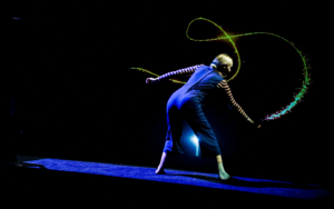 performer for the show ZOOOM, in a dark room creating colorful glow in the dark lines