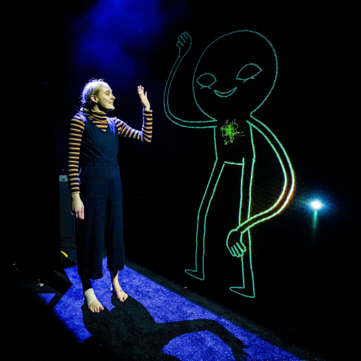 a performer in a dark room, creating a glowing drawing.