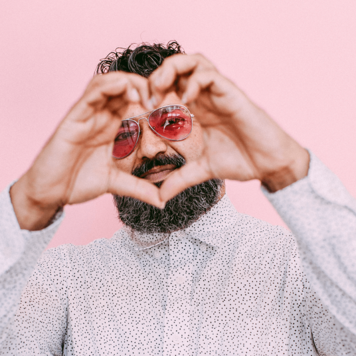 performer Ruploops wearing a white shirt and making a heart shape with their hands, with a pink backdrop