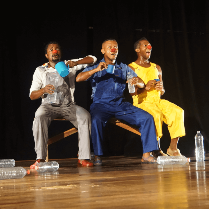 3 performers for the show Sakasaka, on stage, and two of the performers are holding a water bottle and a blue cup in their hand