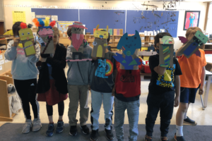students in a classroom holding up the paper puppets they made