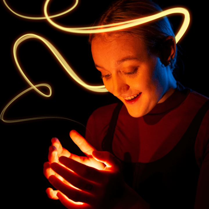 a performer for the show ZOOOM, in a dark room, holding a light in their hands