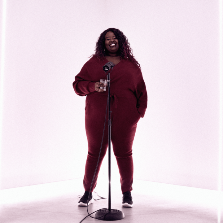 Missy D smiling and standing with a microphone and microphone stand in front of her.