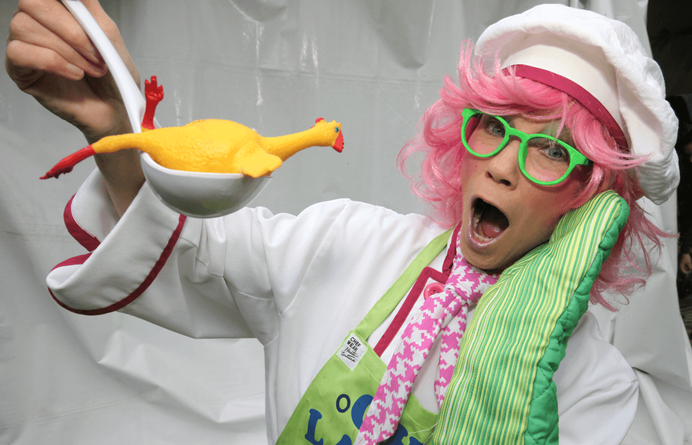 a chef with a shocked face while holding a ladle with a rubber chicken in it
