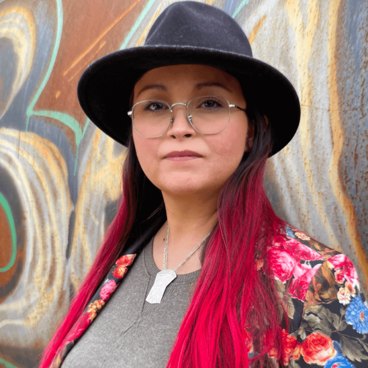 Indigenous Artist Christine Mackenzie in a black hat and grey shirt, with a mural in the background