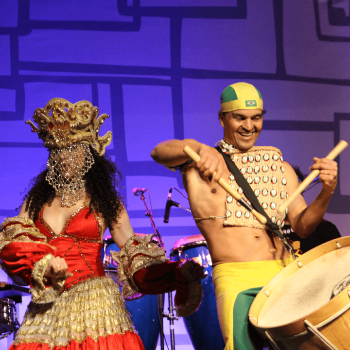 a man playing the drums and a woman in a red dress dancing on stage