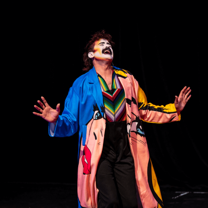 A performer from Glamily in clown makeup, centre stage, wearing colourful robes