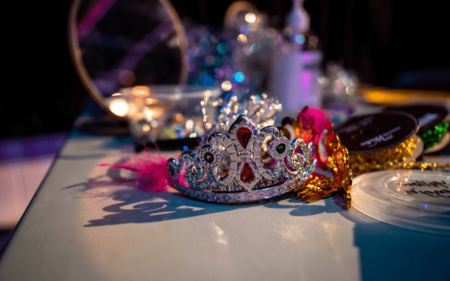 A crown on a table surrounded by feather boas, and other colourful dress-up items.