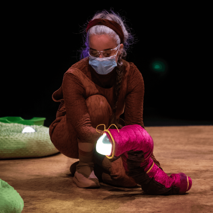 A puppeteer manipulates a pink caterpillar puppet with a glowing light for a face.
