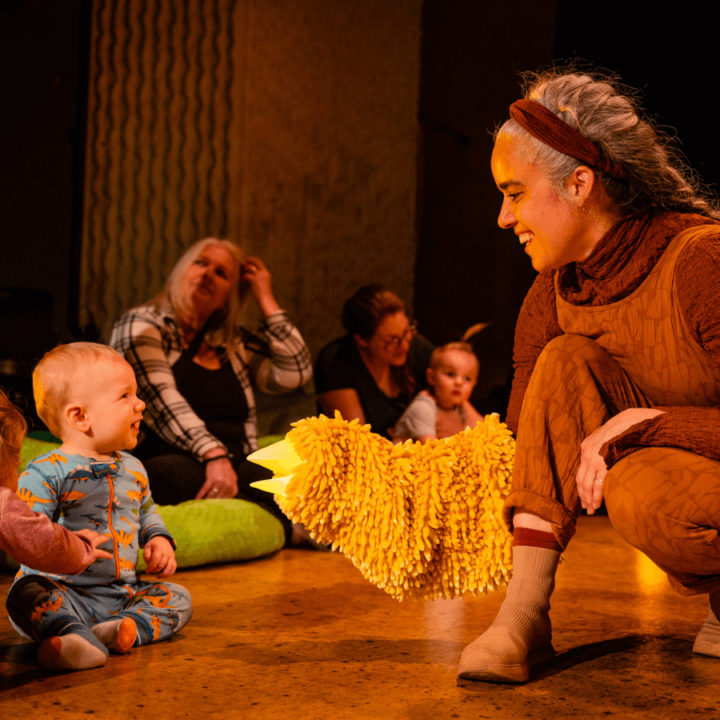 A performer approaching the audience - showing a hand-puppet that looks like a bird to a small child in the front row.