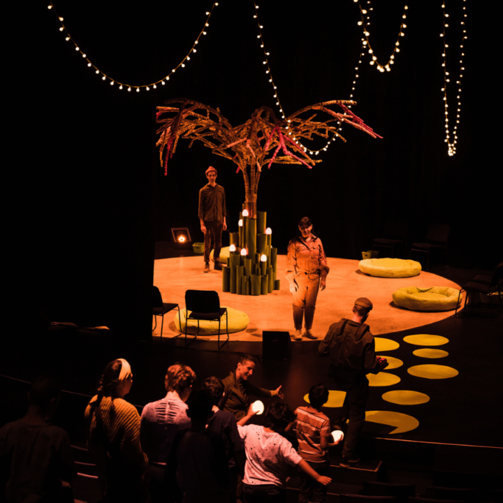 Three performers stand in a line, guiding the audience from their seats up onto the stage.