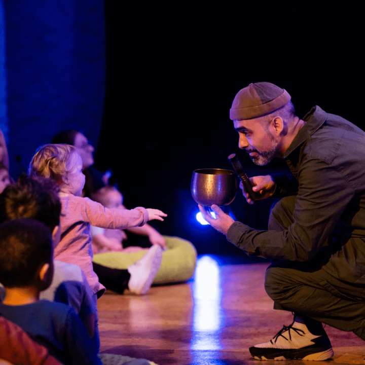 A performer interacting with the audience. He holds a small singing bowl up for a child to see.
