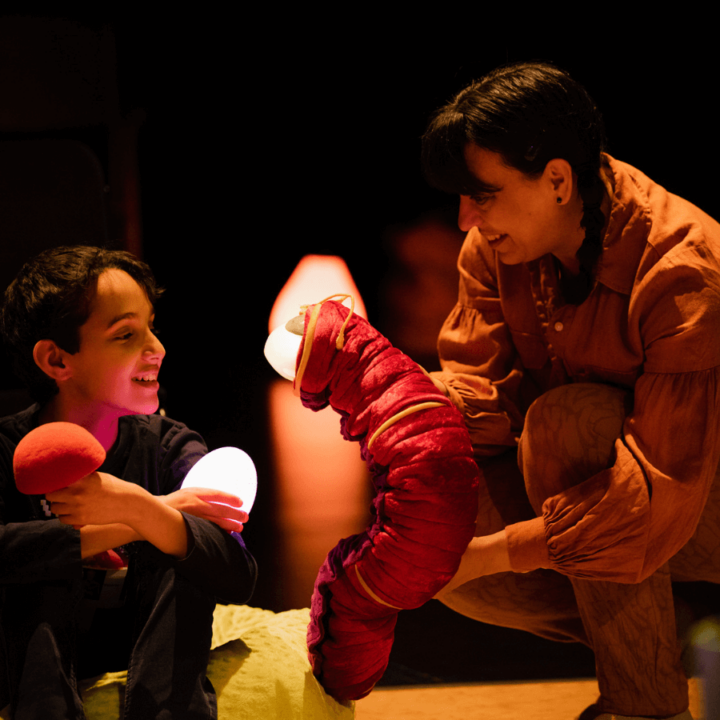 A performer and a child the audience play with colourful, glowing eggs, and a caterpillar hand puppet.