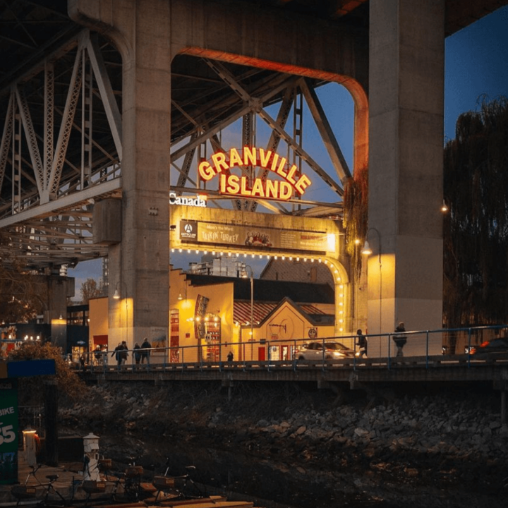 An evening shot of the Granville Island entryway sign. The entrance to Granville Island it lit with warm, yellow fairy lights, covering the entrance archway.