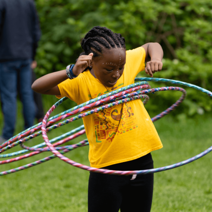 A child playing at the Circus Arts tent in the Activity Village - dancing with multiple hula-hoops around them.