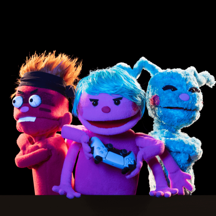 A promotional image for the show "Division Infinity Saves the World" - displaying their three new puppets, Spiderwolf, Chiqui, and Soda. Spiderwolf, the red puppet on the far left of the image has crazy spiked hair and is wearing a sweatband The middle puppet, Soda, poses with her arms around her fellow puppets. Chiqui, the blue puppet on the far right, hugs Soda.