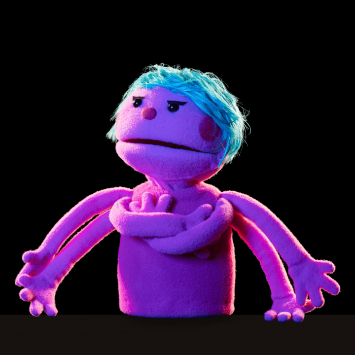 A promotional image for the show "Division Infinity Saves the World" - displaying a purple puppet, with blue hair, named Soda. The puppet poses with their arms crossed.